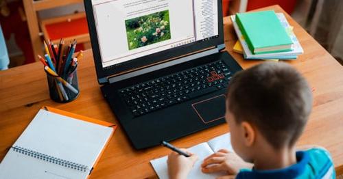 An image of a boy sitting at his desk working on his online class assignments. 